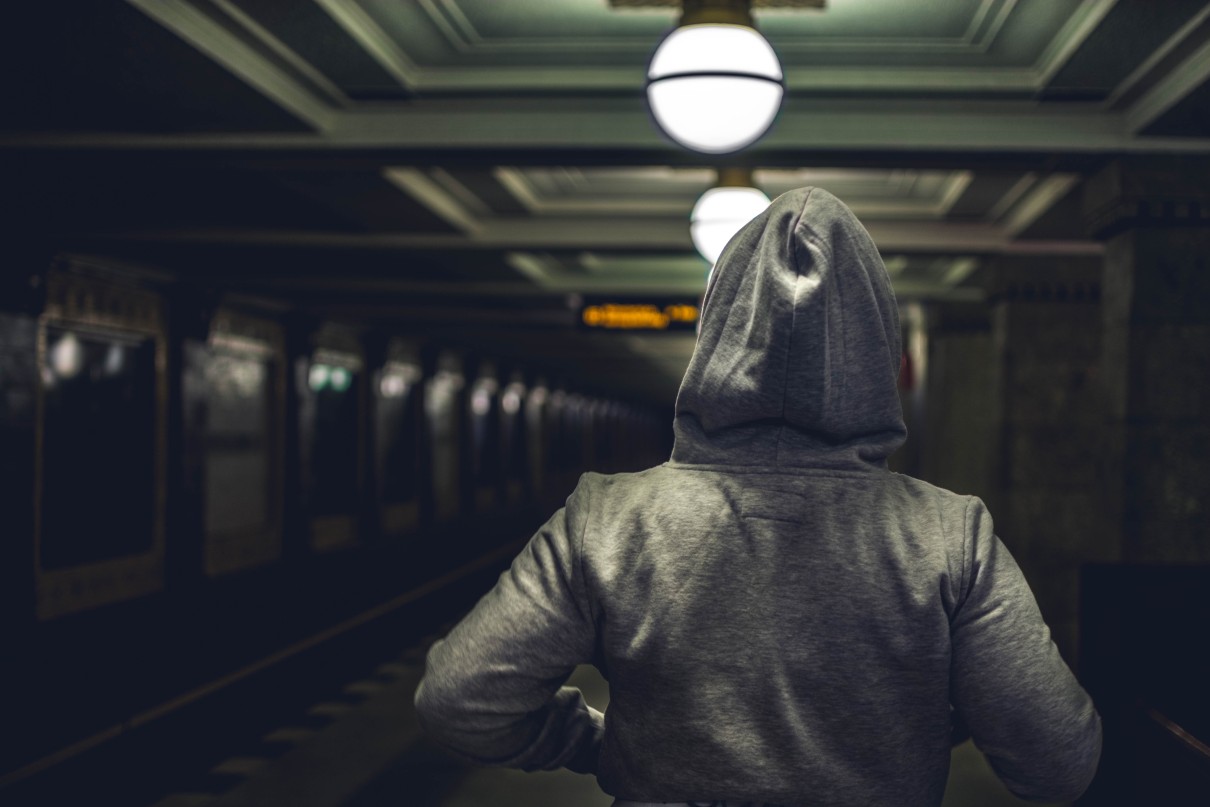 A person in a hoodie is walking on a dark train platform.
