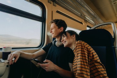 A man and a woman traveling on the train together, smiling.